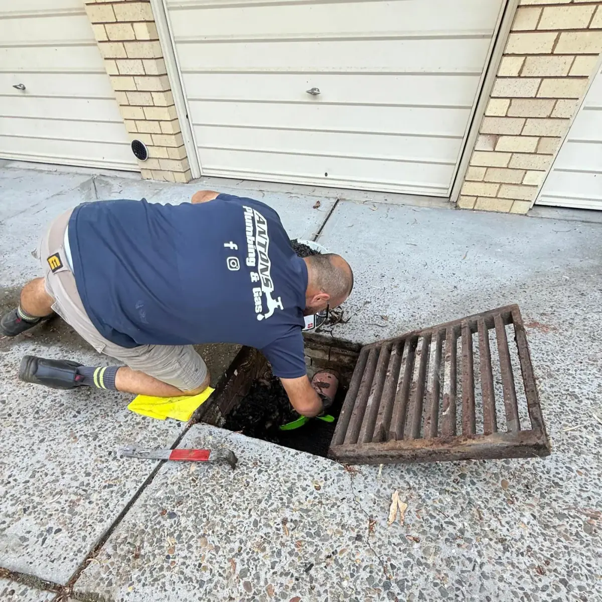 Ryde plumber working inside an open outdoor drain pit beside a garage