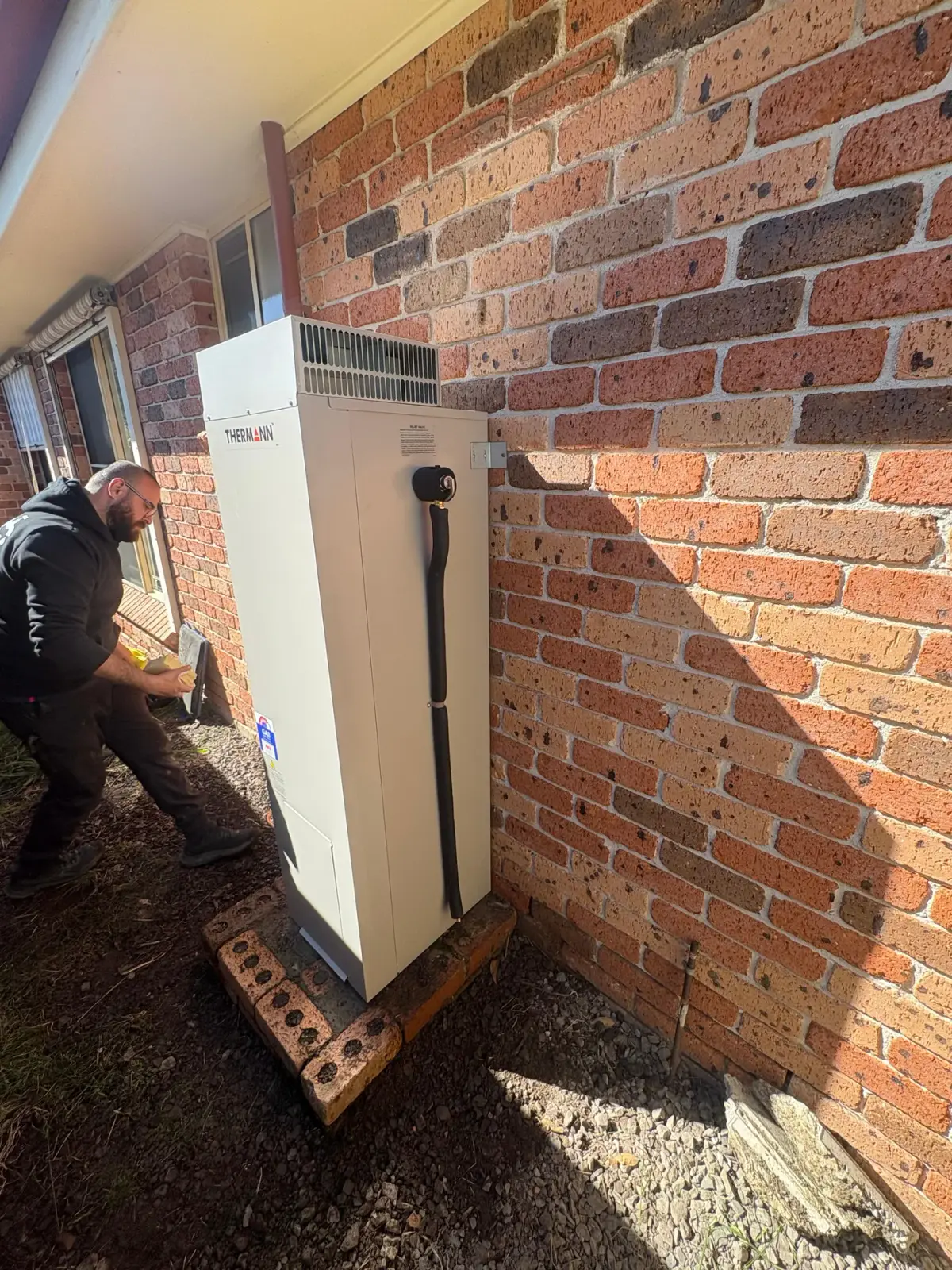 Ryde plumber working beside an outdoor Thermann gas hot water system