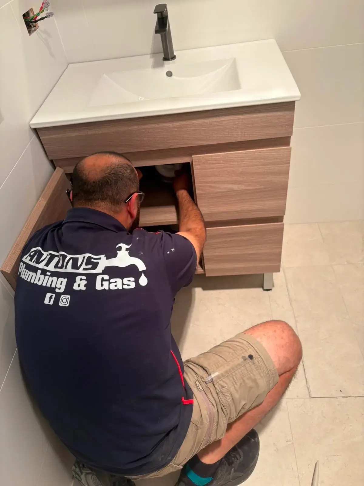 Ryde plumber from Antons repairing pipework beneath a bathroom vanity